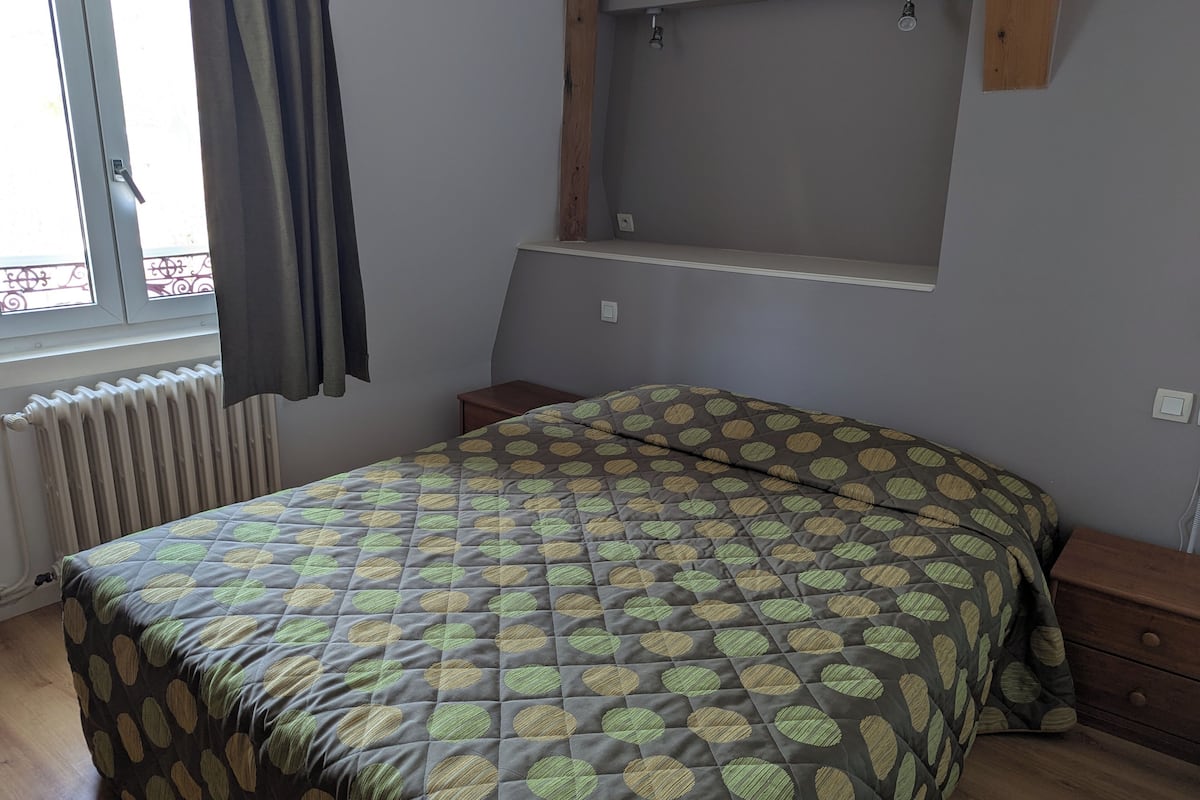 Un dormitorio con cama, ventana con cortinas, radiador y estante de madera.