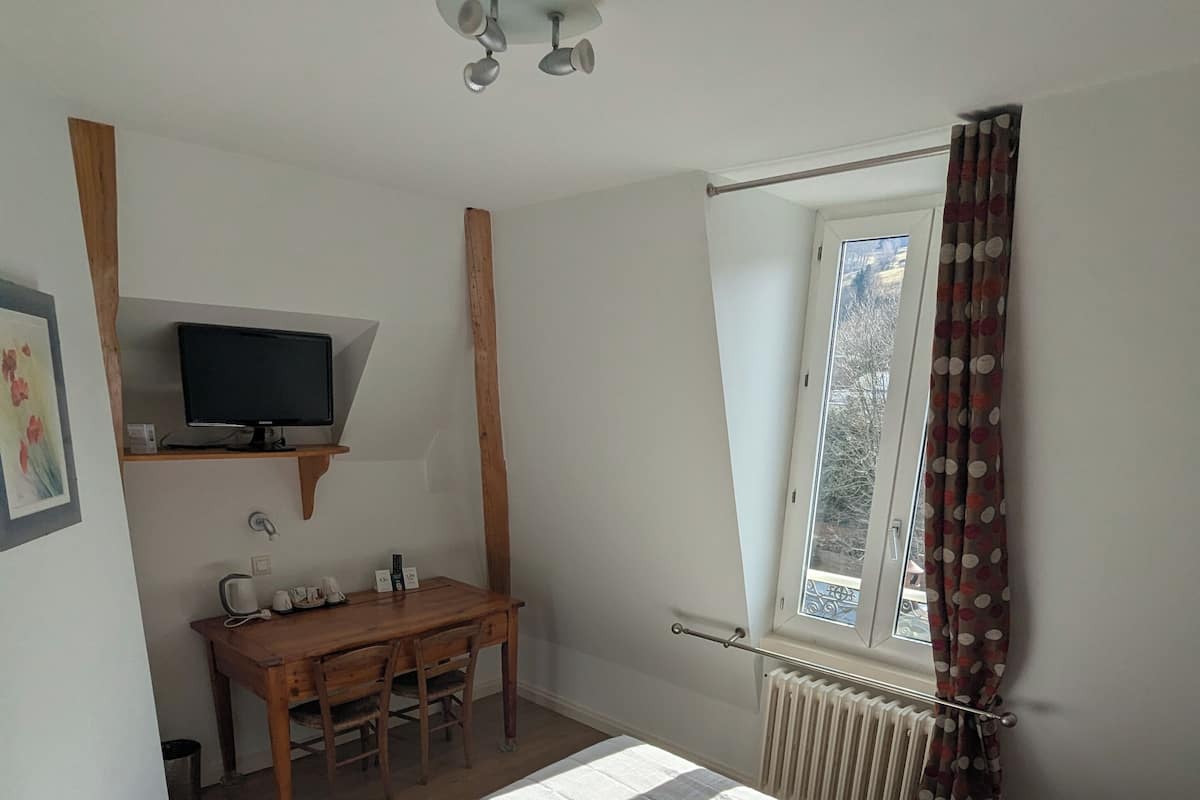 Un dormitorio con una cama, un escritorio con televisor, una ventana con cortinas y un radiador.