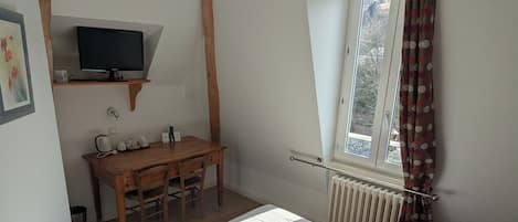 A bedroom with a bed, a desk with a television, a window with curtains, and a radiator.