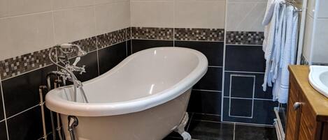 A bathroom with a freestanding bathtub, dark tiled floor, and a wooden vanity with a sink.