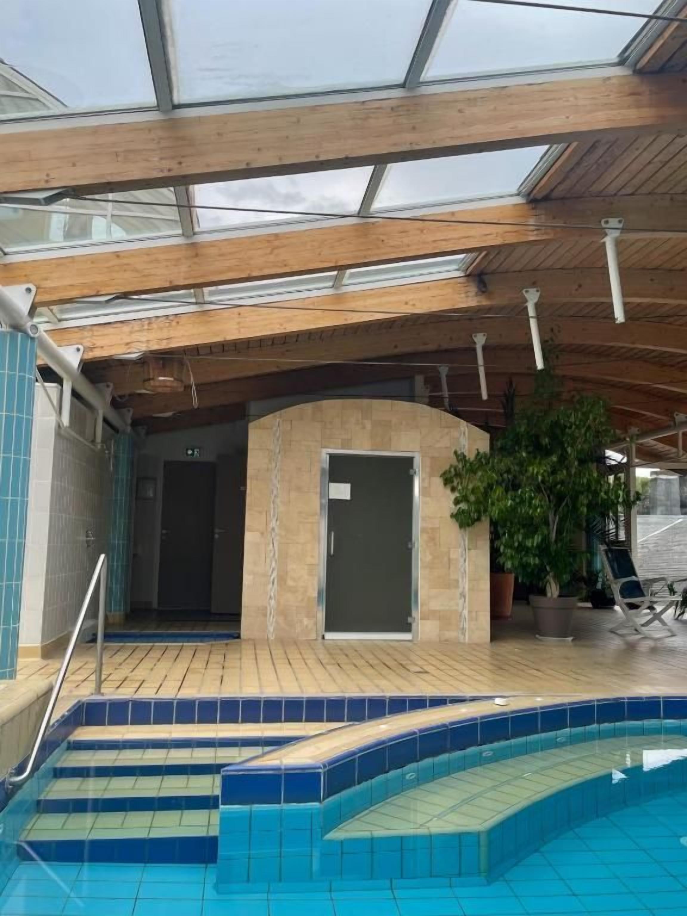 Une piscine intérieure dotée d’un toit en verre, de poutres en bois et d’un sol carrelé.
