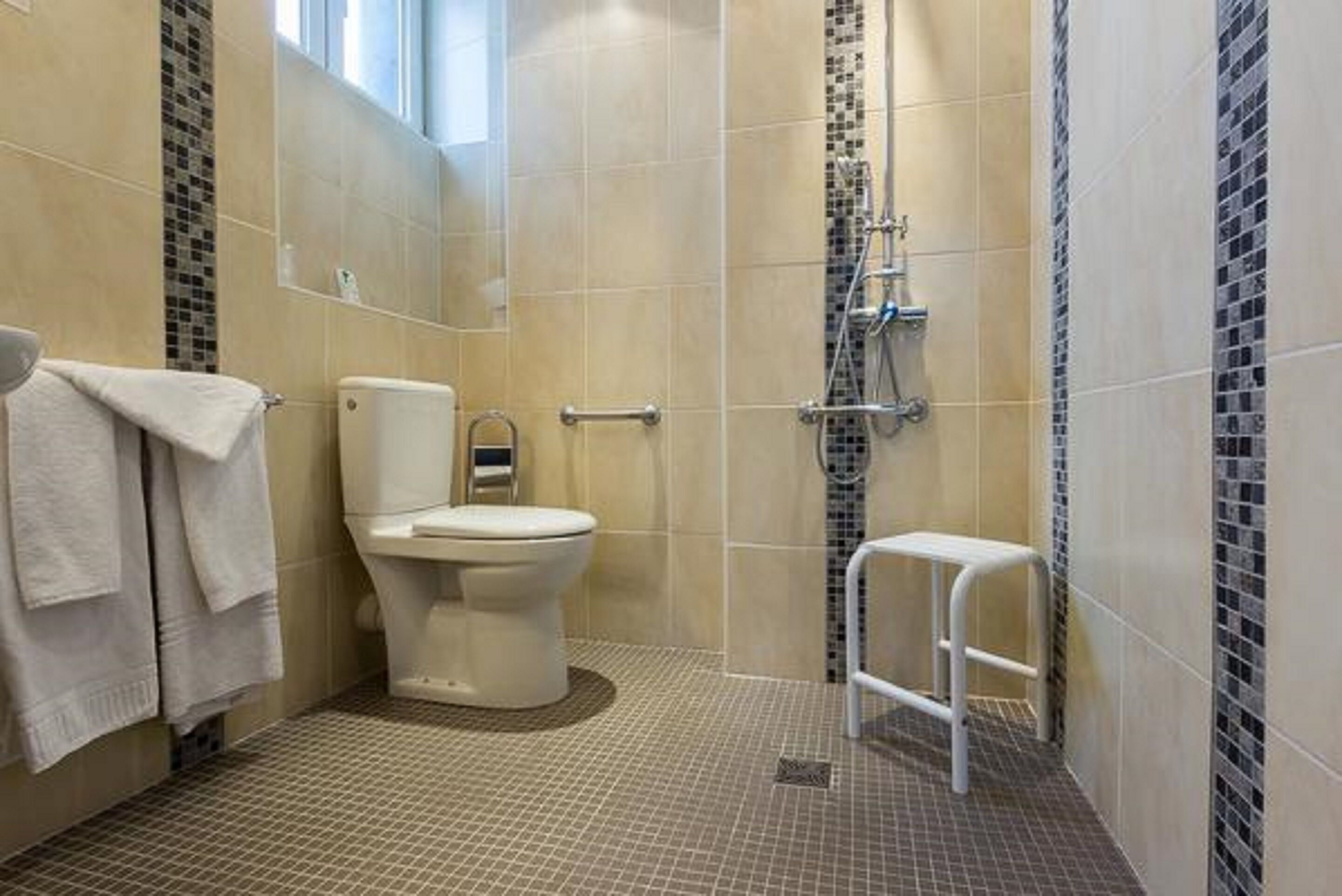 Un baño con inodoro, ducha y un taburete pequeño.