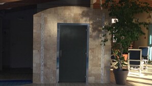 A modern building entrance with a stone facade, a metal door, and a potted plant. - Hôtel Régina (La Bourboule)