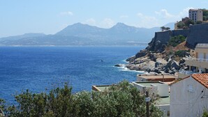 Vista costera con mar azul cristalino, terreno rocoso y un edificio con techo de tejas.