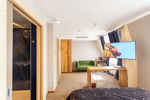 A bedroom with a bed, a desk, a chair, a green armchair, a television, and a wardrobe.