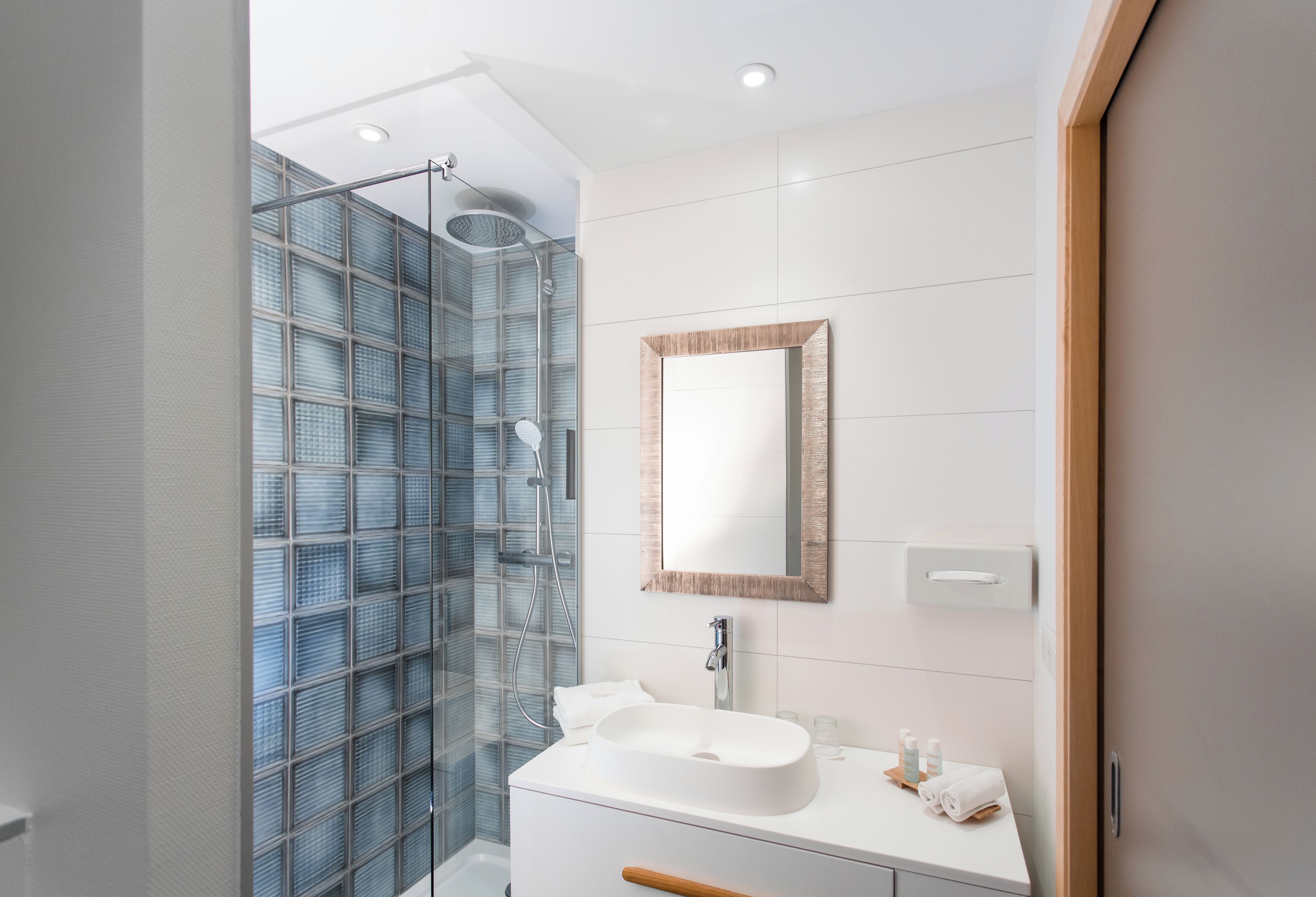 A modern bathroom with a glass shower enclosure, a white sink, and a mirror with a wooden frame.