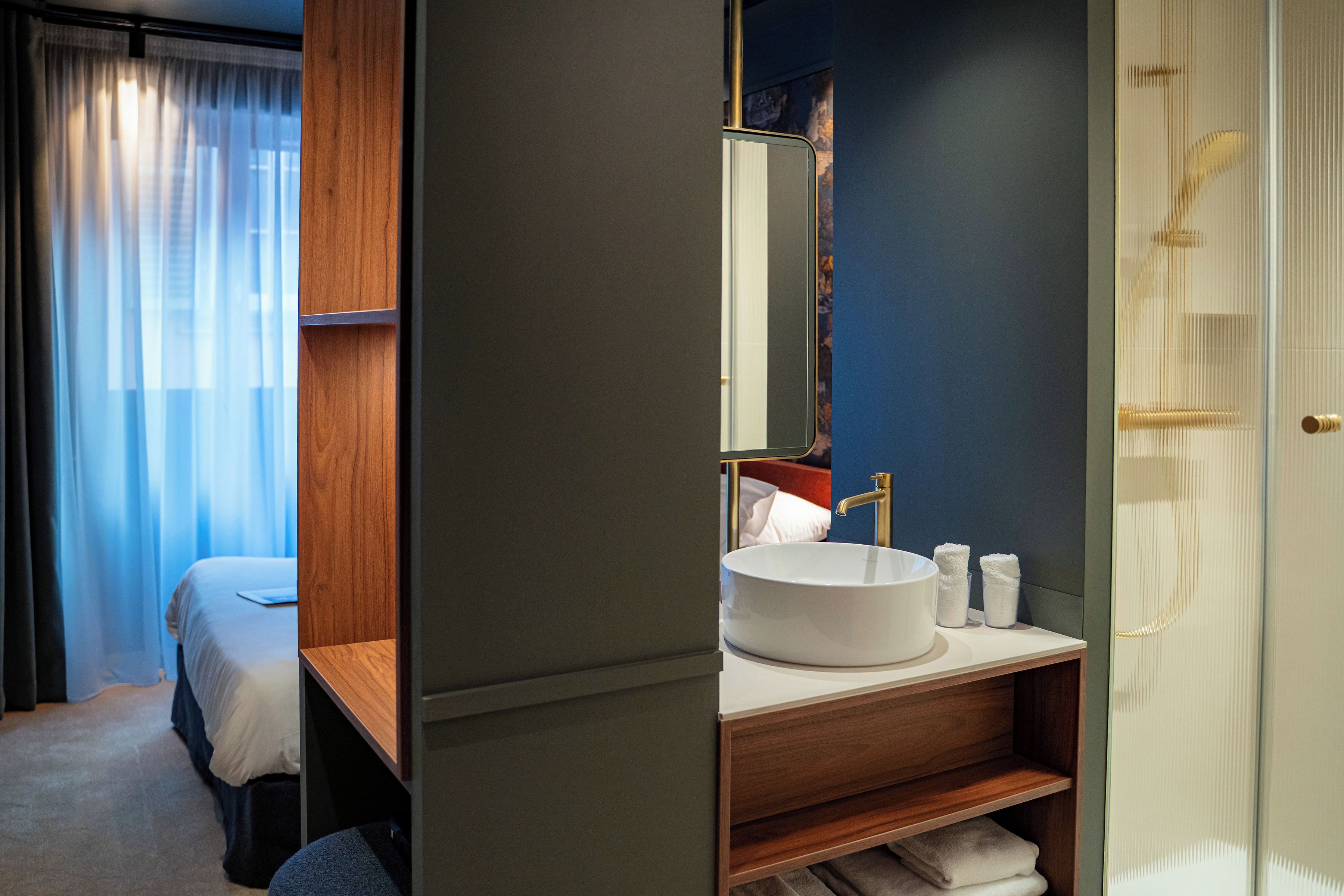 Una habitación de hotel moderna con una cama grande, un tocador de madera con lavabo y una ducha.
