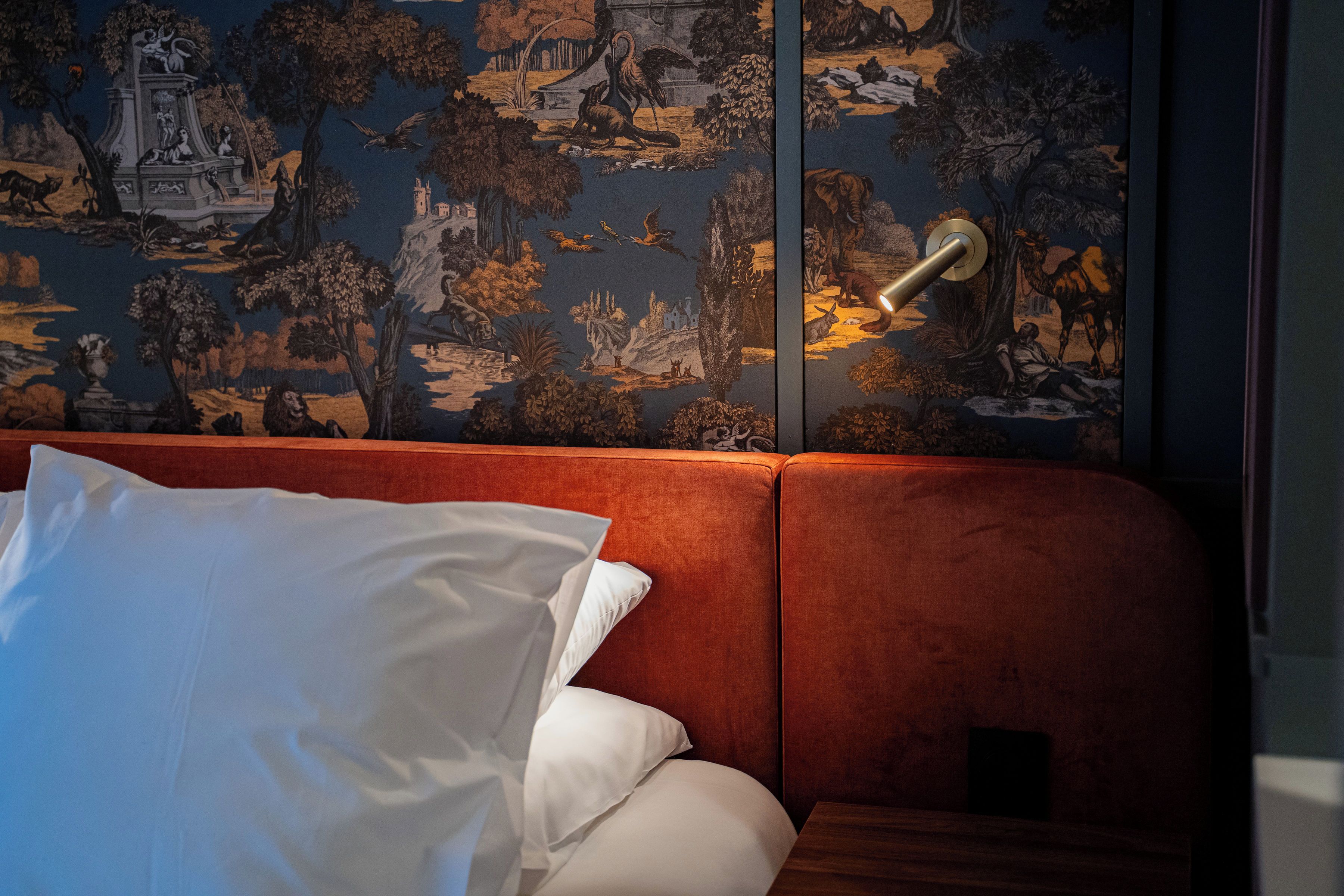 A room with a red upholstered sofa, white pillows, and a wall with a detailed mural.