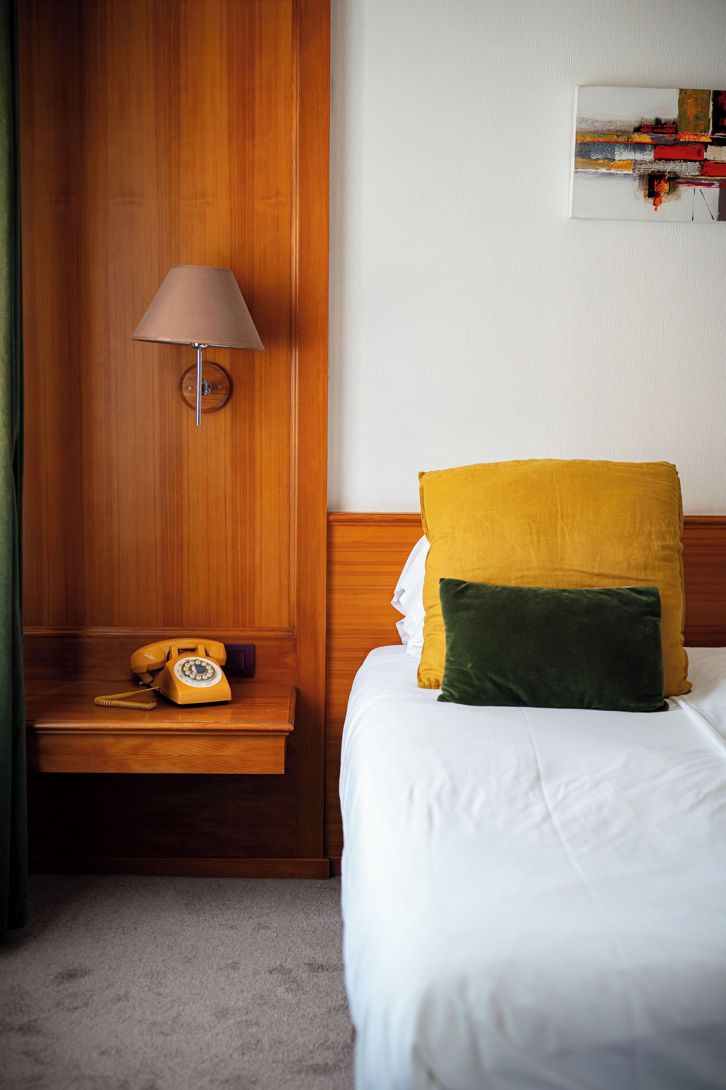 Une chambre d’hôtel avec une tête de lit en bois, une table de chevet avec une lampe, un téléphone et deux oreillers.
