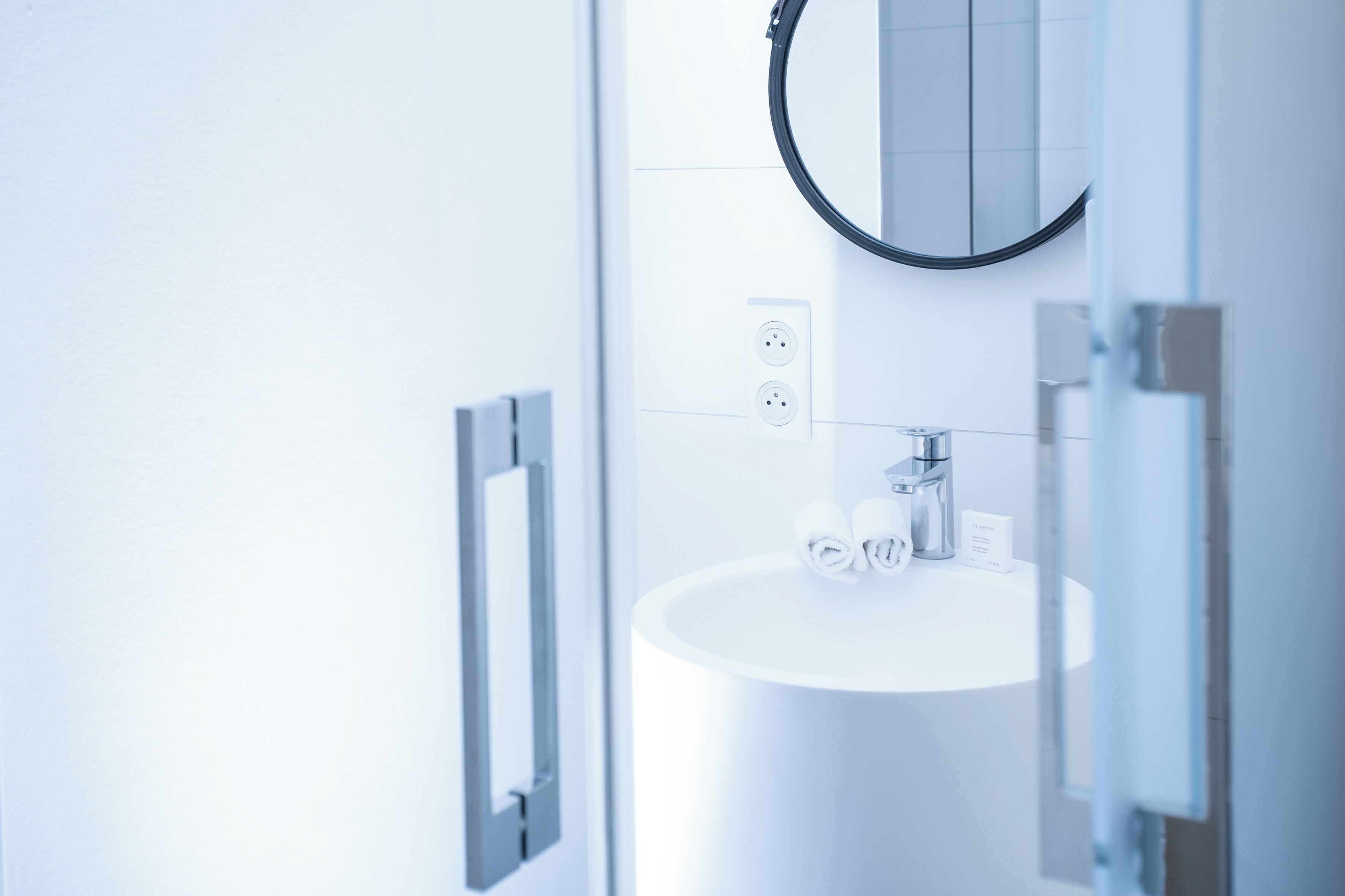 A modern bathroom with a white sink, a round mirror, and a glass shower enclosure.