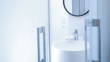 A modern bathroom with a white sink, a round mirror, and a glass shower enclosure.