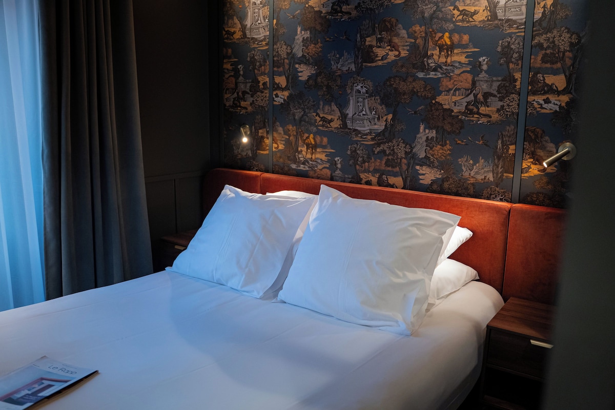 A hotel room with a bed, white linens, a wooden headboard, and a wall with a detailed mural.