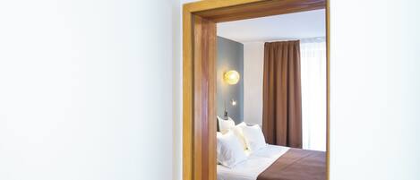 A hotel room with a bed, a nightstand, a wall-mounted lamp, and a window with curtains.