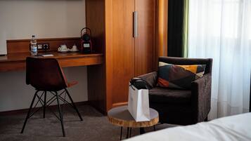 A hotel room with a wooden desk, a chair, a small round table, a bed, and a window with curtains.