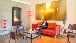 A modern lounge area with a fireplace, a red sofa, a glass table with a teapot, and a chessboard. - La Fischhutte, The Originals Relais (Mollkirch)
