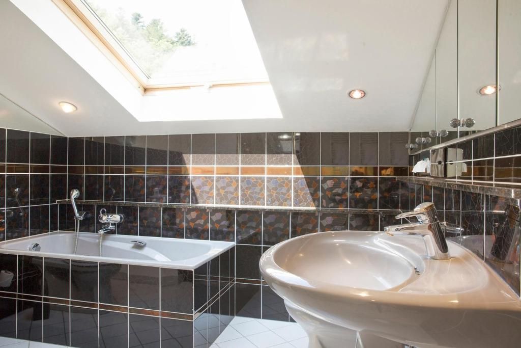A modern bathroom with a skylight, a bathtub, and a large sink.