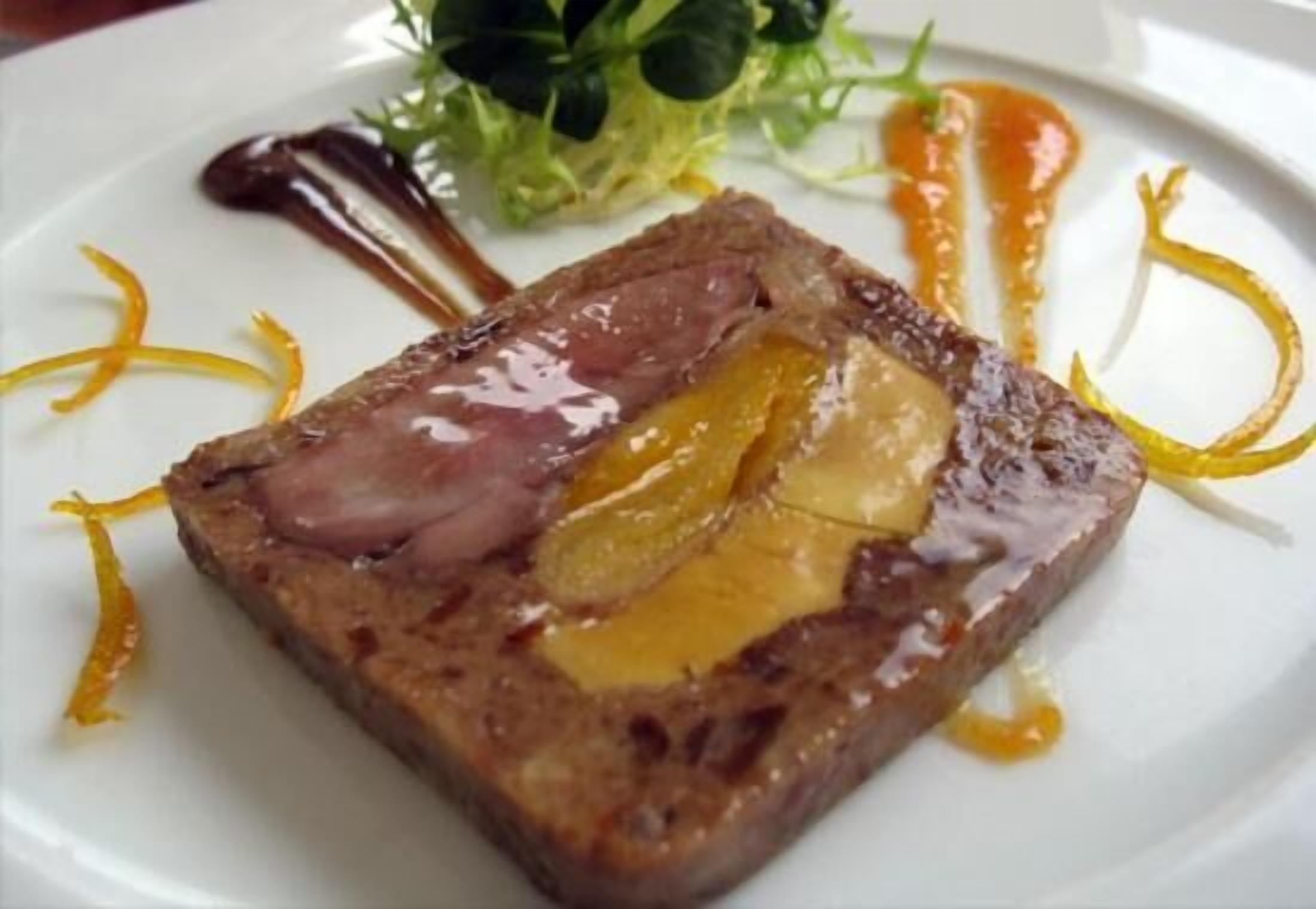 Piatto impiattato con una fetta di carne, probabilmente manzo, guarnita con una fetta di frutta e un filo di salsa.
