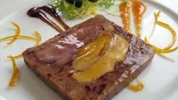 Piatto impiattato con una fetta di carne, probabilmente manzo, guarnita con una fetta di frutta e un filo di salsa.