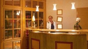A reception desk with wooden panels, glass doors, and pendant lighting. - La Fischhutte, The Originals Relais (Mollkirch)