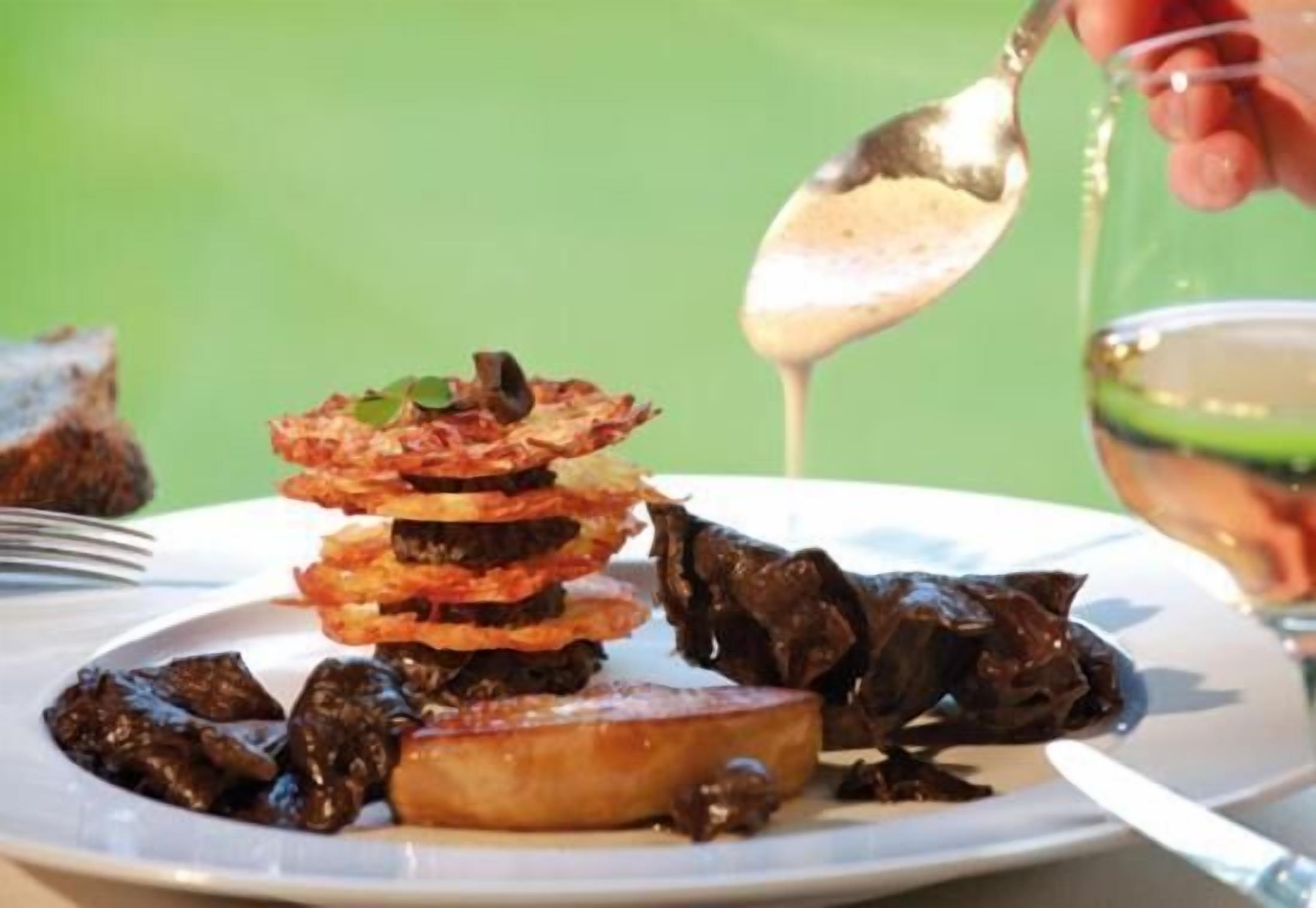 A plate of food with a variety of items including what appears to be fried plantains, a piece of meat, and a dark sauce being poured over it.