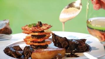 A plate of food with a variety of items including what appears to be fried plantains, a piece of meat, and a dark sauce being poured over it.