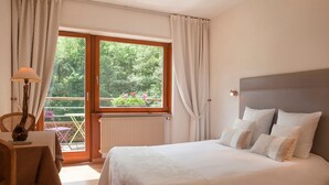 A bedroom with a large bed, a desk, and a view of a balcony with outdoor furniture. - La Fischhutte, The Originals Relais (Mollkirch)