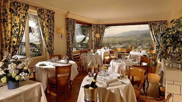 A restaurant with multiple tables set for dining, a view of the countryside, and floral decorations. - Le Clos Saint Vincent (Ribeauvillé)