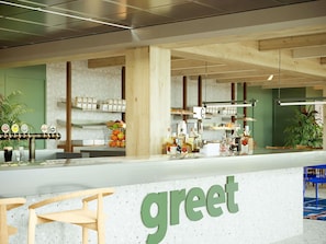 Un mostrador con un letrero que dice 'greet', estantes con bebidas y una zona de estar.