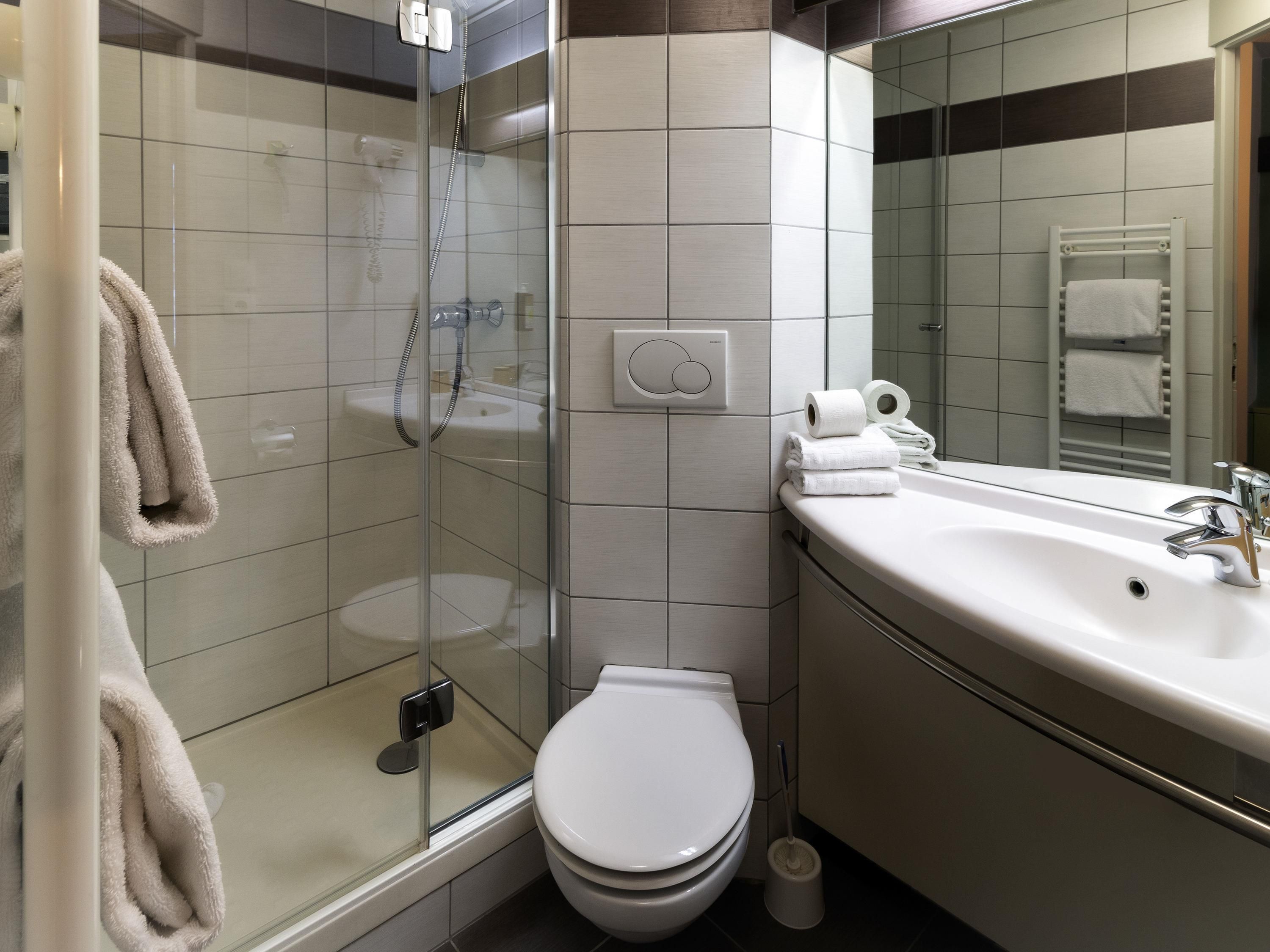 A modern bathroom with a glass-enclosed shower, a white toilet, and a sink with a mirror above it.