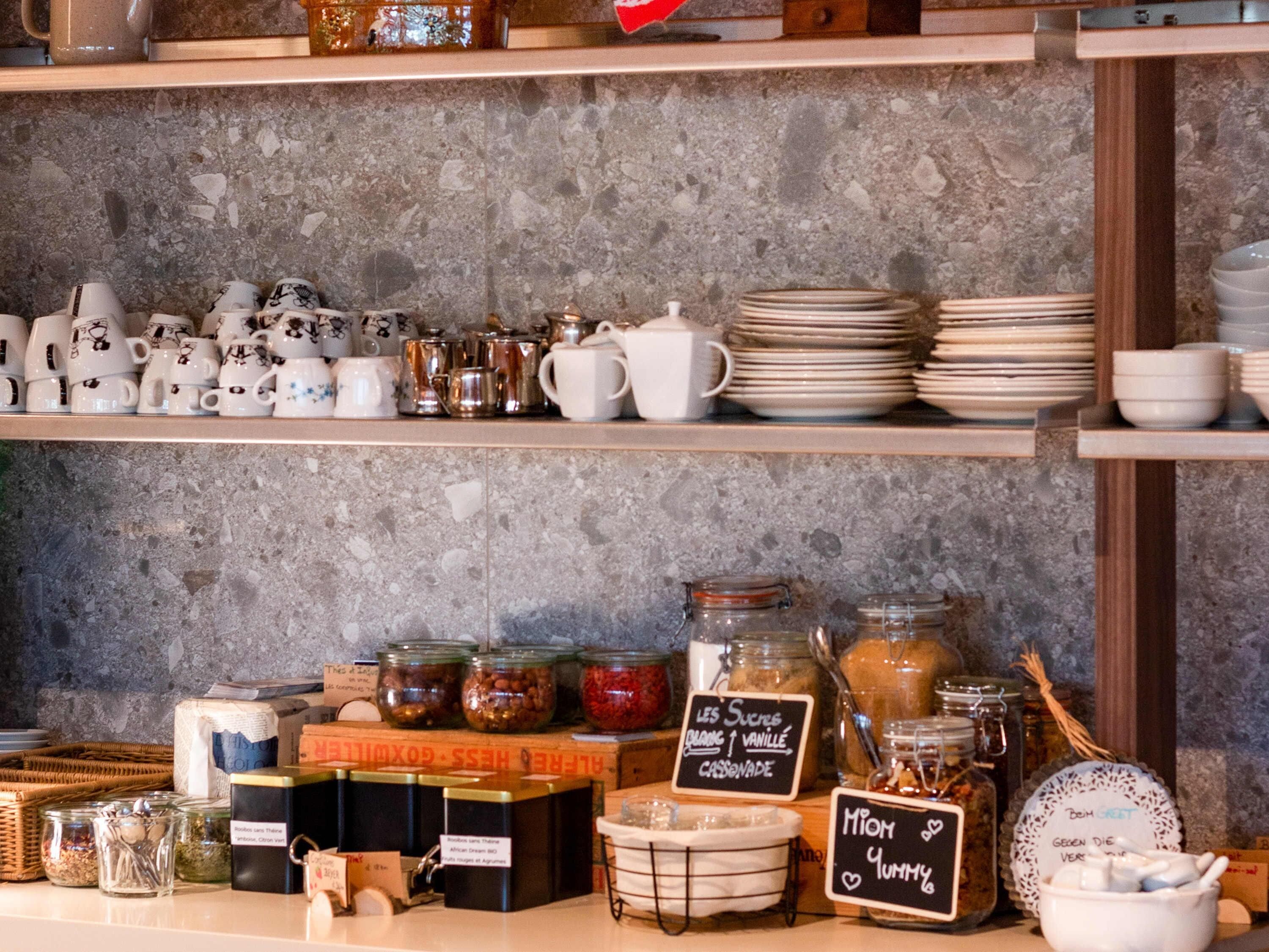 A kitchen counter with various kitchenware, including mugs, teapots, and plates, and jars of spices and condiments.