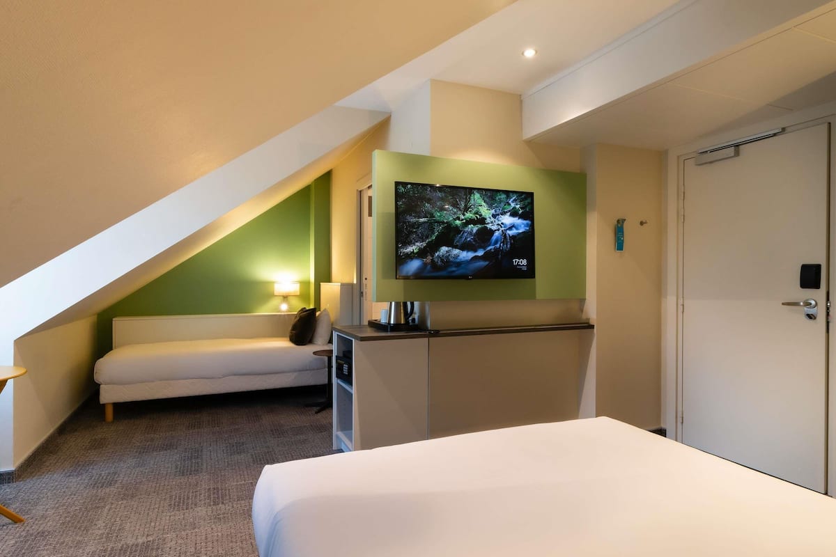 A hotel room with a bed, a TV mounted on the wall, a sofa, and a desk.