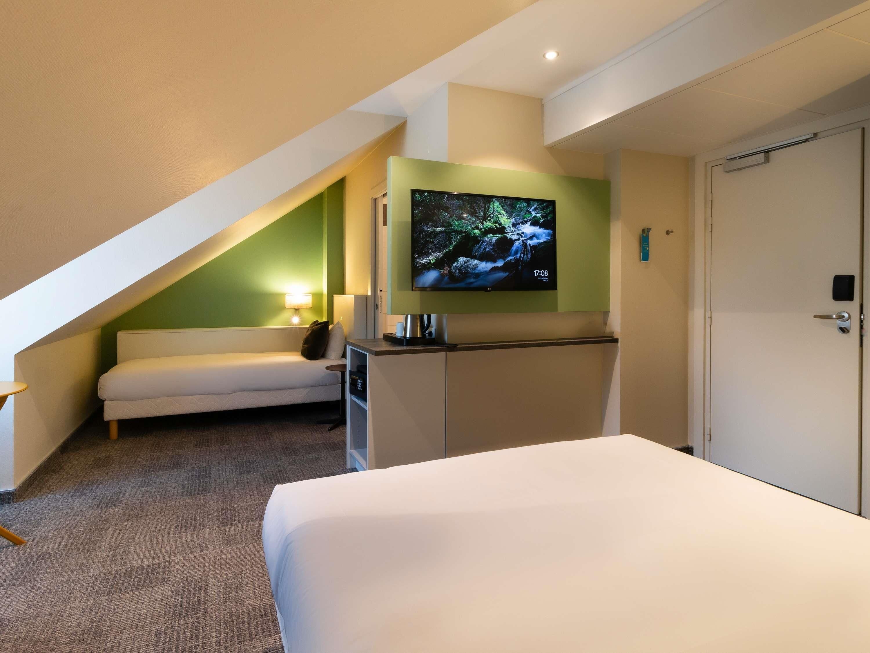 Une chambre d’hôtel équipée d’un lit, d’un téléviseur fixé au mur, d’un canapé et d’un bureau.