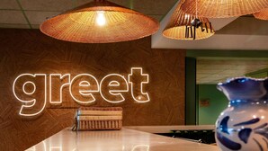 Un mostrador de recepción con un cartel que dice 'greet', lámparas de mimbre y un jarrón.