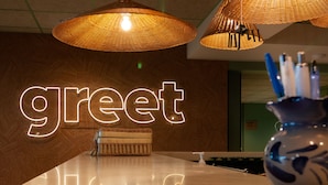 A reception area with a 'greet' sign, wicker pendant lights, a reception desk, and a vase with pens. - greet Hôtel Colmar (Colmar)