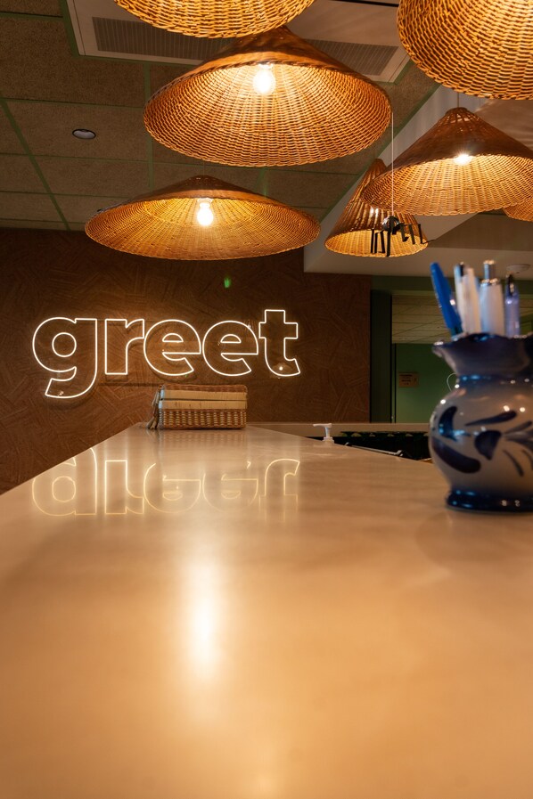A reception area with a 'greet' sign, wicker pendant lights, a reception desk, and a vase with pens. - greet Hôtel Colmar (Colmar)