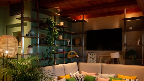 Una sala de estar acogedora con un sofá modular, un sillón de ratán, una mesa de centro y estantes con adornos.