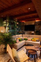 Una sala de estar acogedora con un sofá modular, un sillón de ratán, una mesa de centro y estantes con adornos.