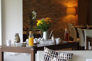 A breakfast table set with a coffee pot, teapot, cups, a glass pitcher of orange juice, and a vase of flowers. - Hôtel Jenny (Hagenthal-le-Bas)