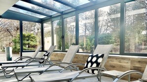 A sunroom with large windows, reclining chairs, and a wooden bench. - Hôtel Jenny (Hagenthal-le-Bas)
