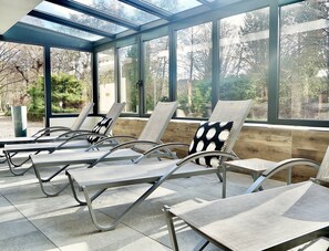 A sunroom with large windows, reclining chairs, and a wooden bench. - Hôtel Jenny (Hagenthal-le-Bas)