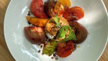 Une assiette blanche contenant une variété de légumes rôtis et un petit morceau de viande, le tout agrémenté d’une feuille, posée sur une table en bois.