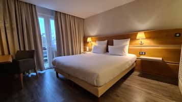 A hotel room with a large bed, two bedside lamps, a chair, and a view of the outdoors through a window with curtains.