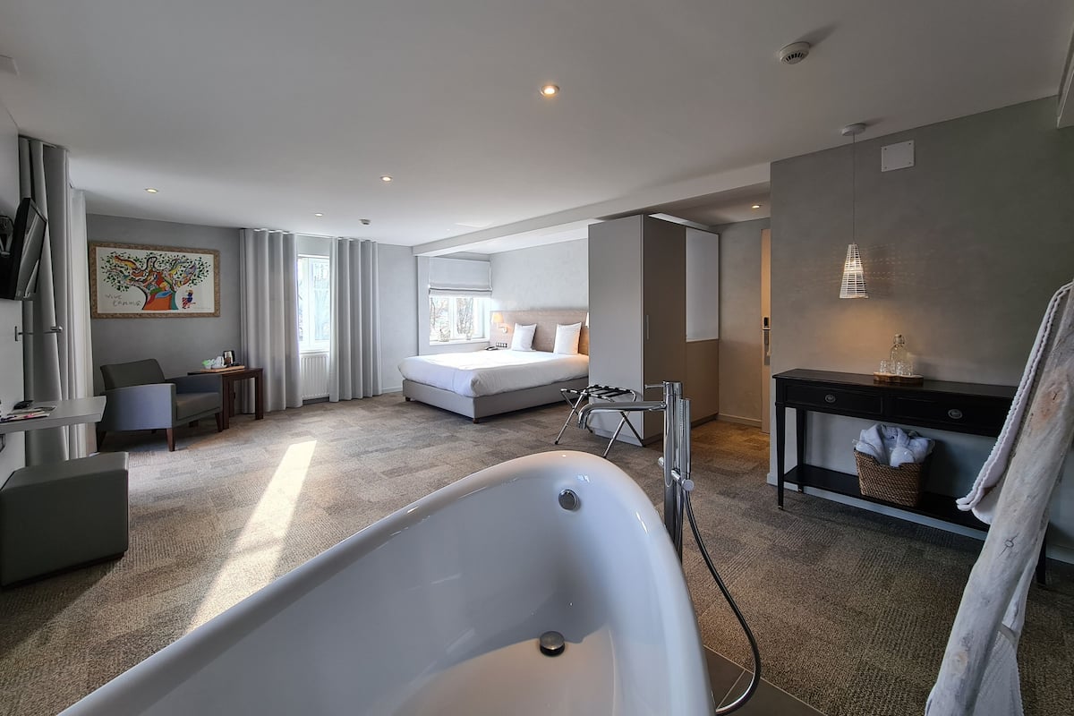 Et moderne hotelværelse med et stort badekar, en seng, et skrivebord og en stol.