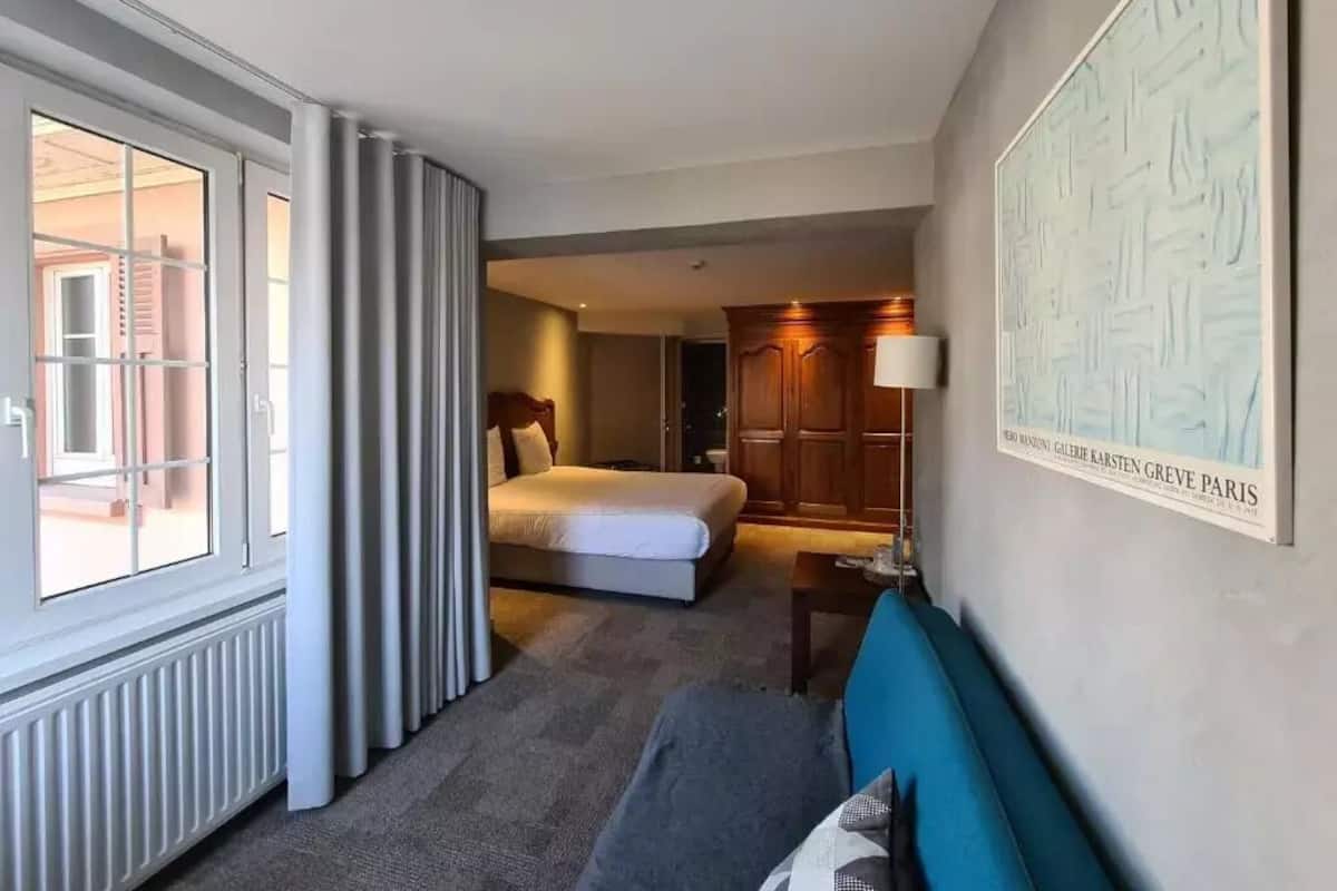 Et hotelværelse med en seng, en sofa, en lampe og et stort vindue.