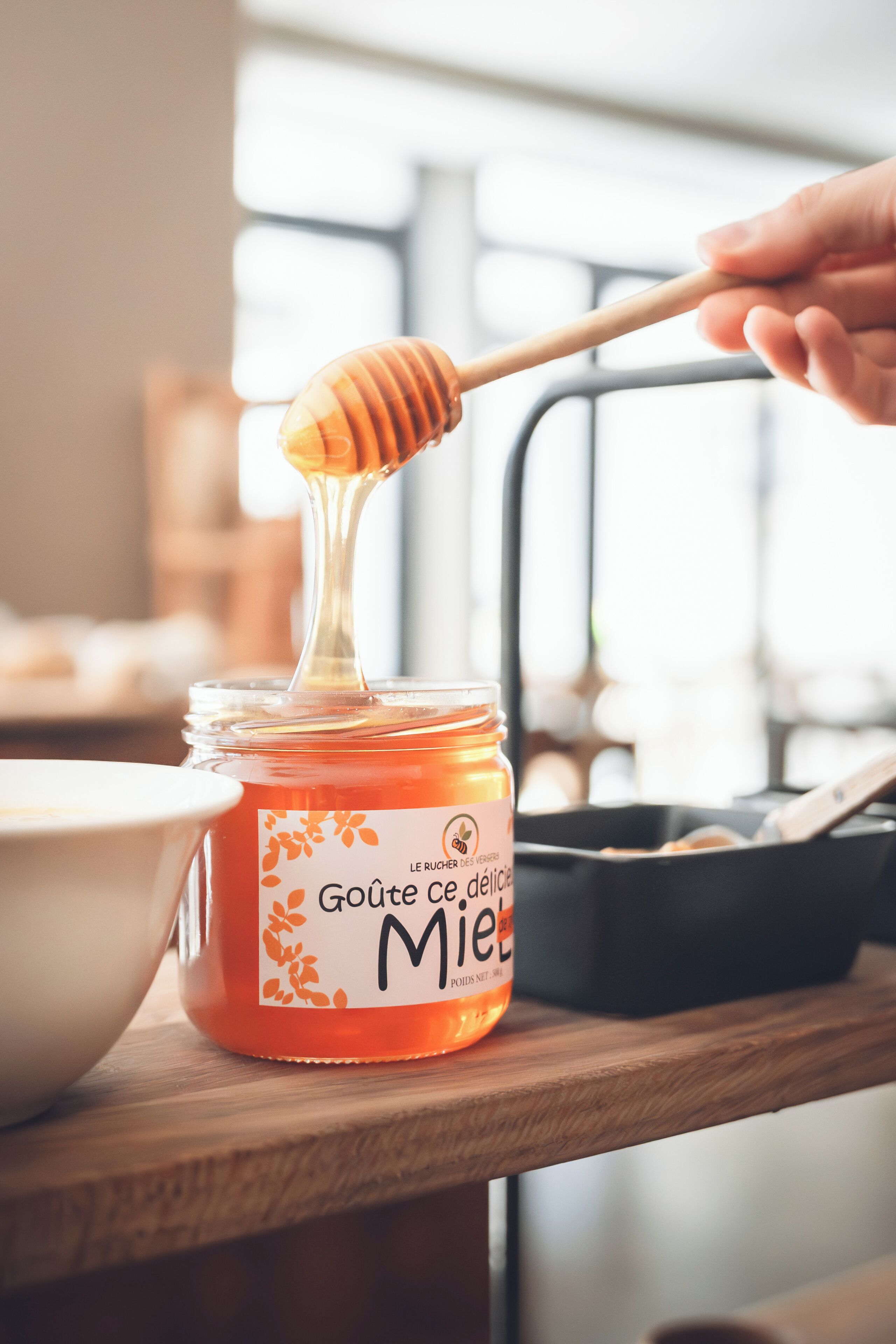 A jar of honey with a honey dipper on a wooden surface.
