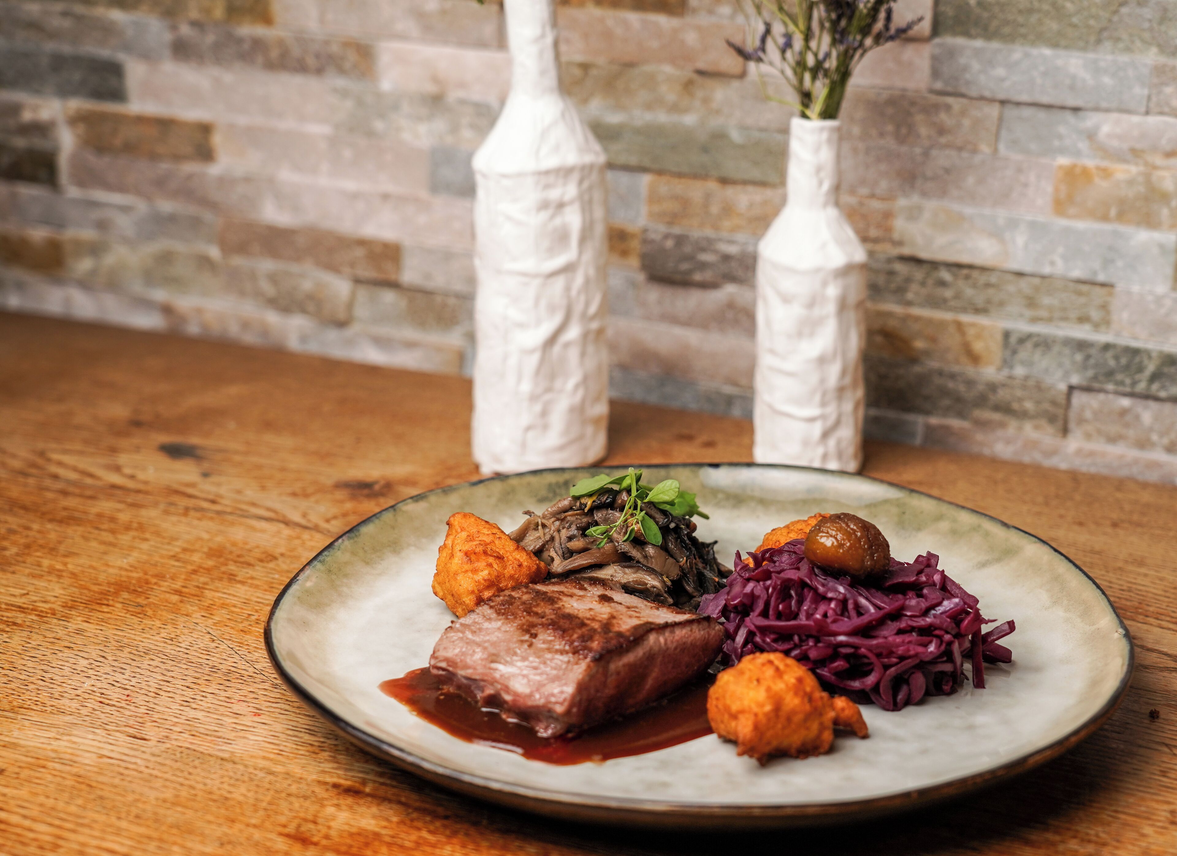 A plate of food with a steak, vegetables, and a sauce on a wooden table.