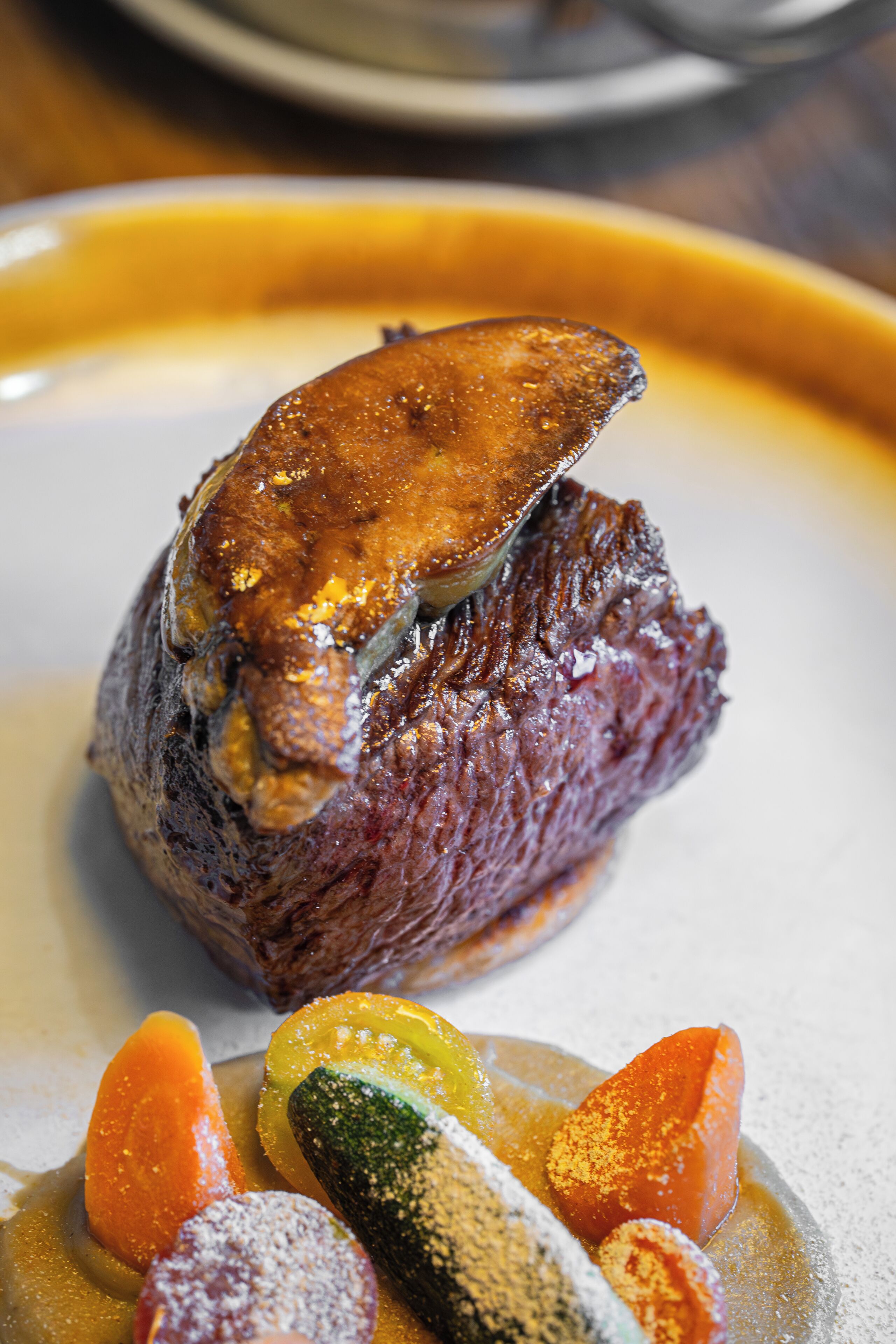 Ein Steak mit glänzender, karamellisierter Kruste, dazu verschiedene Gemüsesorten und eine Soße.
