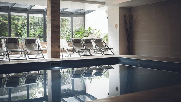 Un'area piscina moderna in interno, con poltrone relax e ampie finestre.