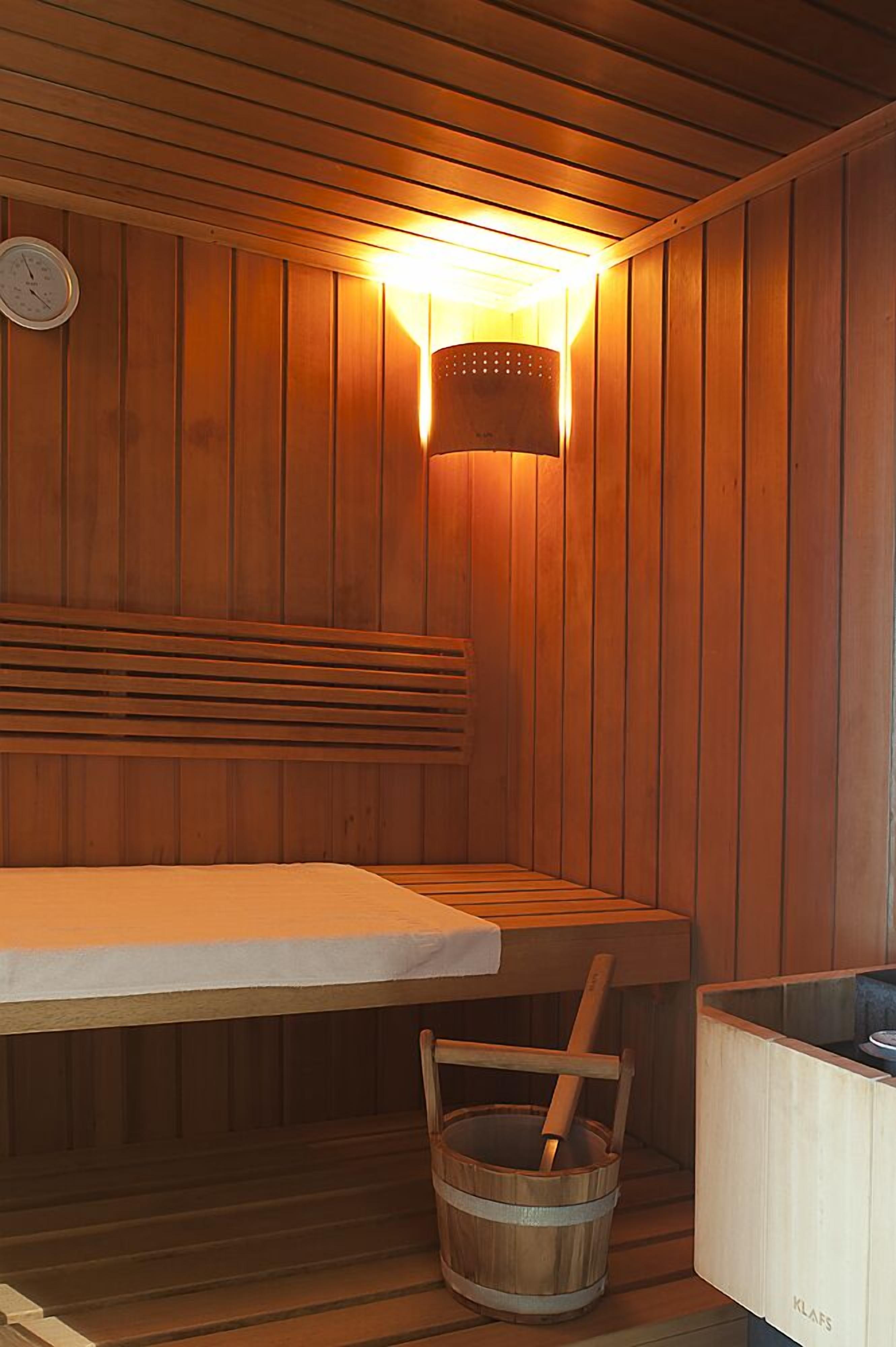 A sauna with wooden walls, a bench, a bucket, and a wall-mounted heater.