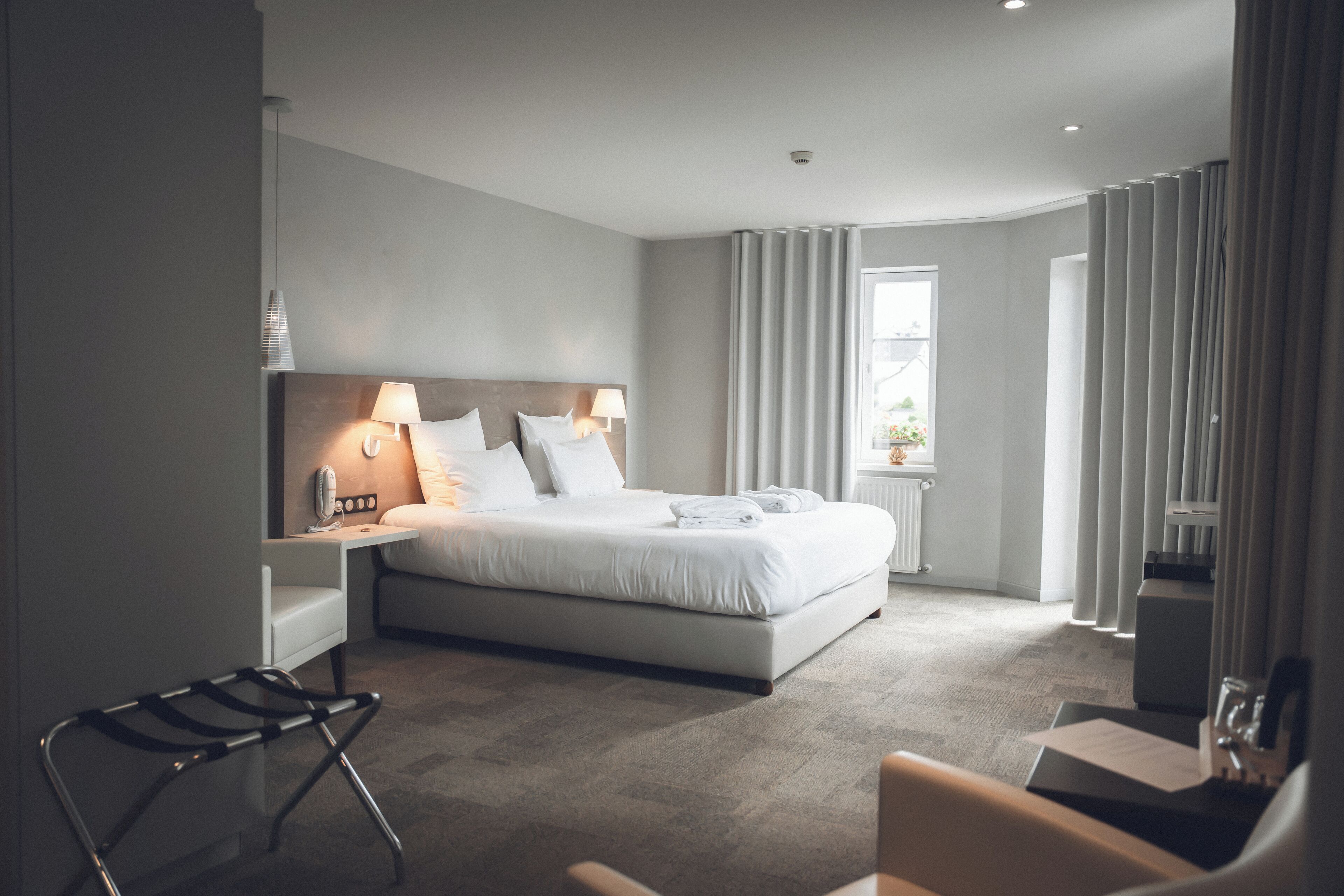 Una habitación de hotel moderna con cama, lámparas de noche, una silla y un ventanal con cortinas.